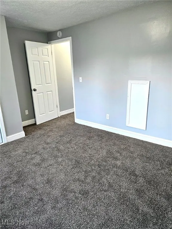 Empty room with carpet flooring, baseboards, a textured ceiling, and a smoke detector
