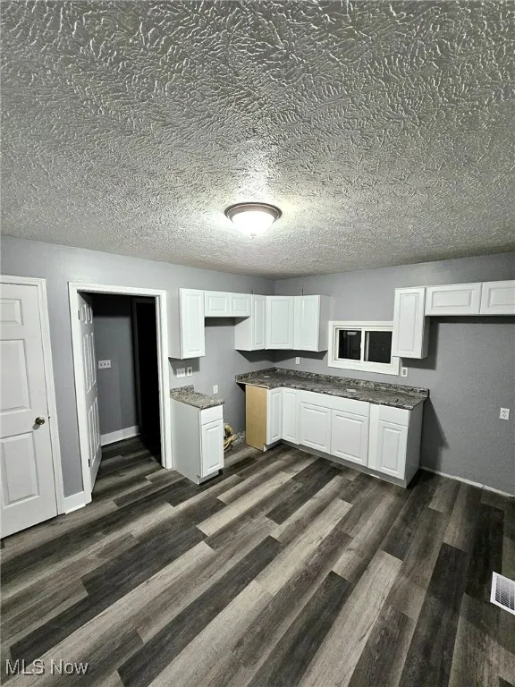 Kitchen featuring dark wood-style flooring, white cabinetry, a textured ceiling, and stone counters