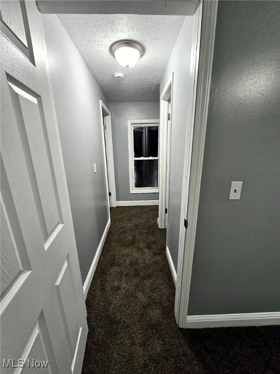 Hall featuring baseboards, carpet, and a textured ceiling