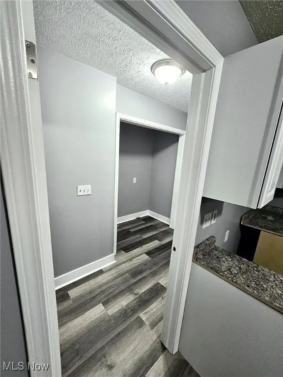 Corridor with dark wood-style floors, baseboards, and a textured ceiling