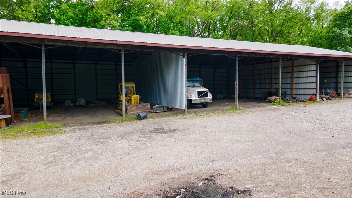 View of car parking featuring a pole building, a detached carport, dirt driveway, and view of wooded area