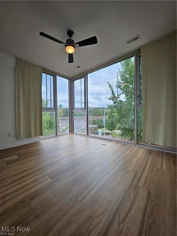 Spare room with wood finished floors, a ceiling fan, and floor to ceiling windows