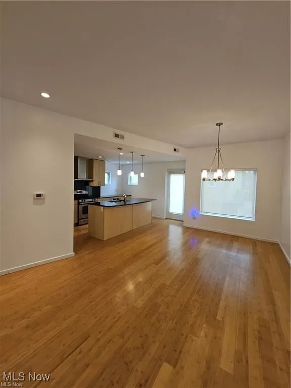 Kitchen featuring open floor plan, dark countertops, a chandelier, light wood-type flooring, and stainless steel range with gas stovetop