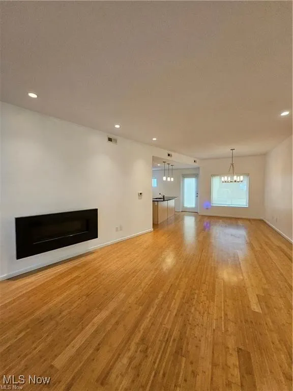 Unfurnished living room featuring light wood finished floors, a fireplace, a chandelier, recessed lighting, and baseboards