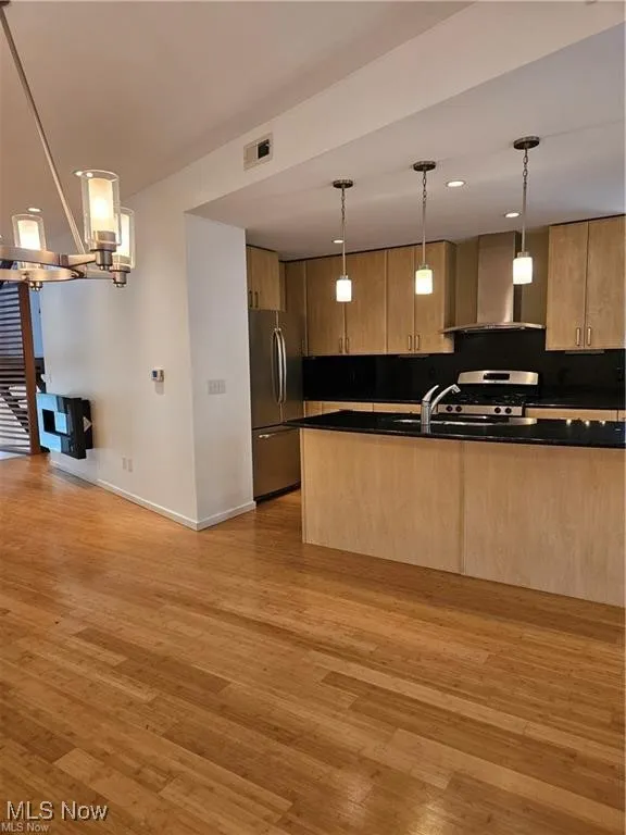 Kitchen featuring appliances with stainless steel finishes, dark countertops, wall chimney range hood, light wood-style flooring, and recessed lighting