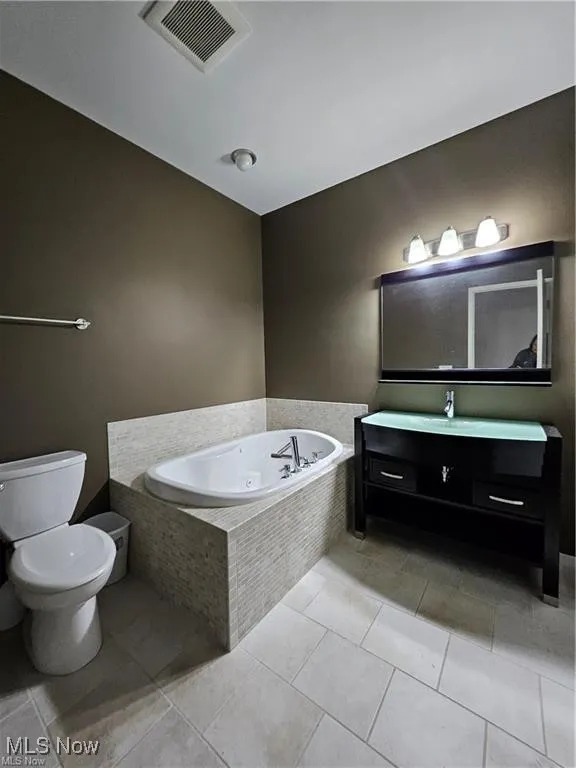 Full bath featuring a jetted tub, toilet, vanity, and tile patterned floors