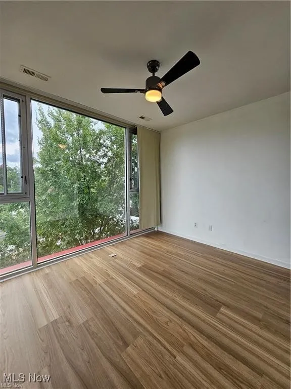 Unfurnished room with floor to ceiling windows, wood finished floors, a ceiling fan, and baseboards