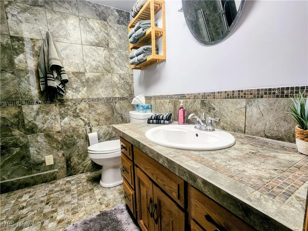 Bathroom with vanity, toilet, and tile walls