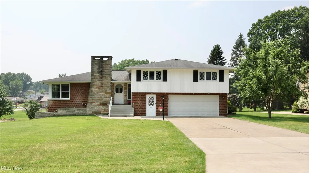 Split level home with an attached garage, brick siding, concrete driveway, and a front lawn