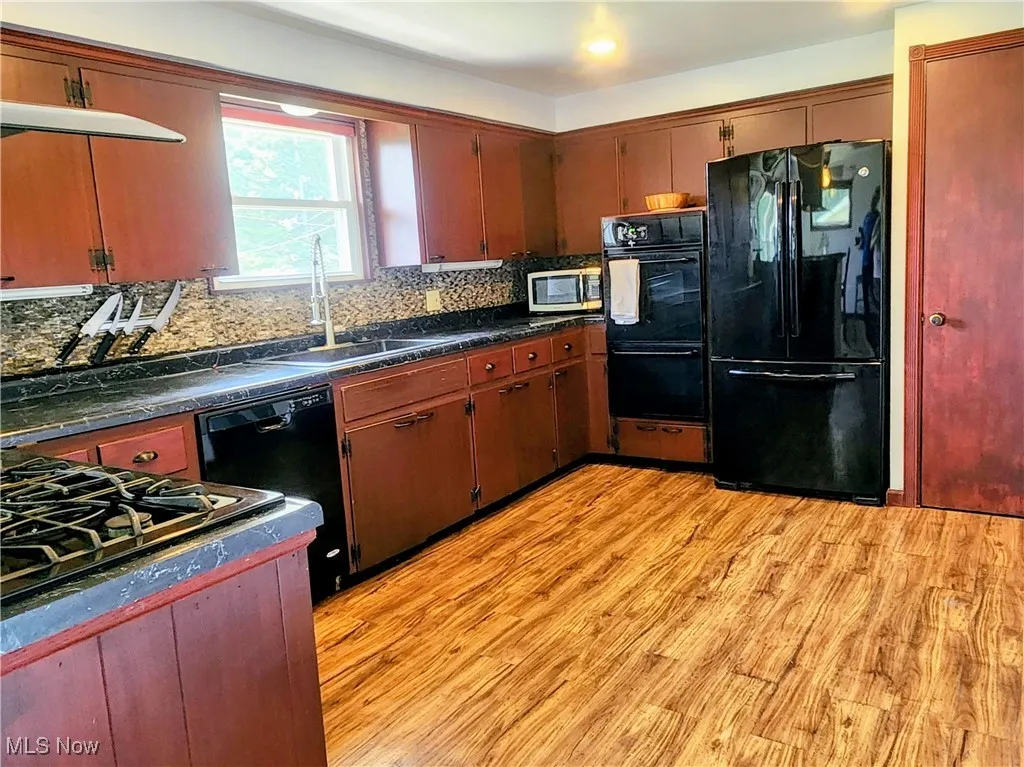 Kitchen with black appliances, a sink, dark countertops, and tasteful backsplash
