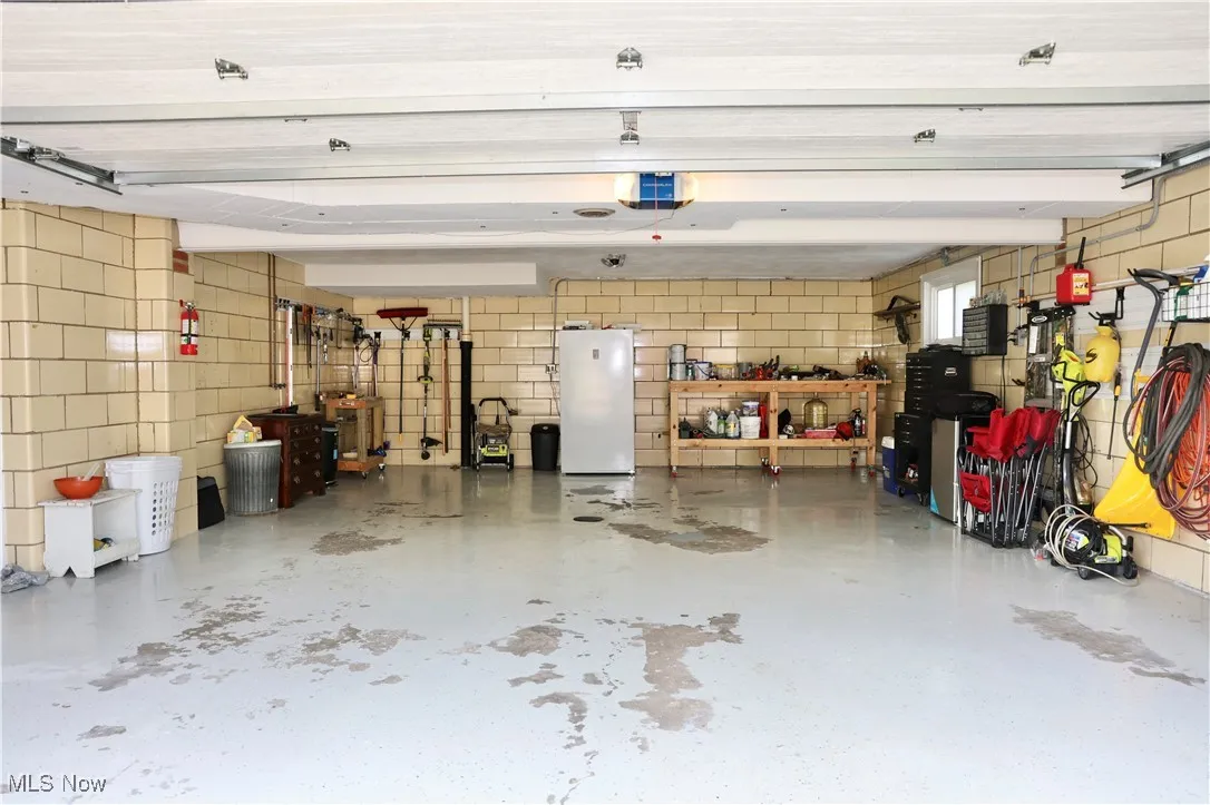 Garage with freestanding refrigerator, a garage door opener, and concrete block wall