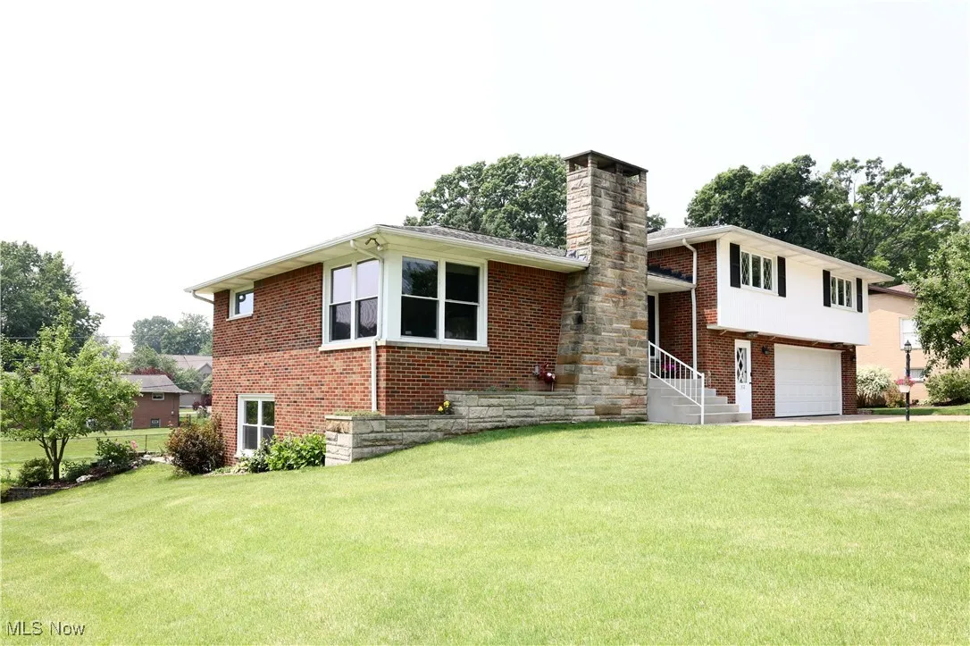 Split level home with an attached garage, brick siding, a front yard, and a chimney