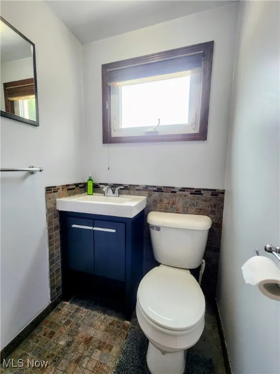 Half bathroom with tile walls, vanity, toilet, and a wainscoted wall