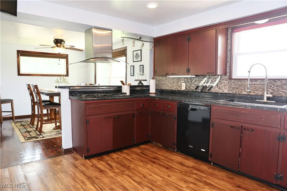 Kitchen with island exhaust hood, dishwasher, a sink, dark wood-style flooring, and dark countertops