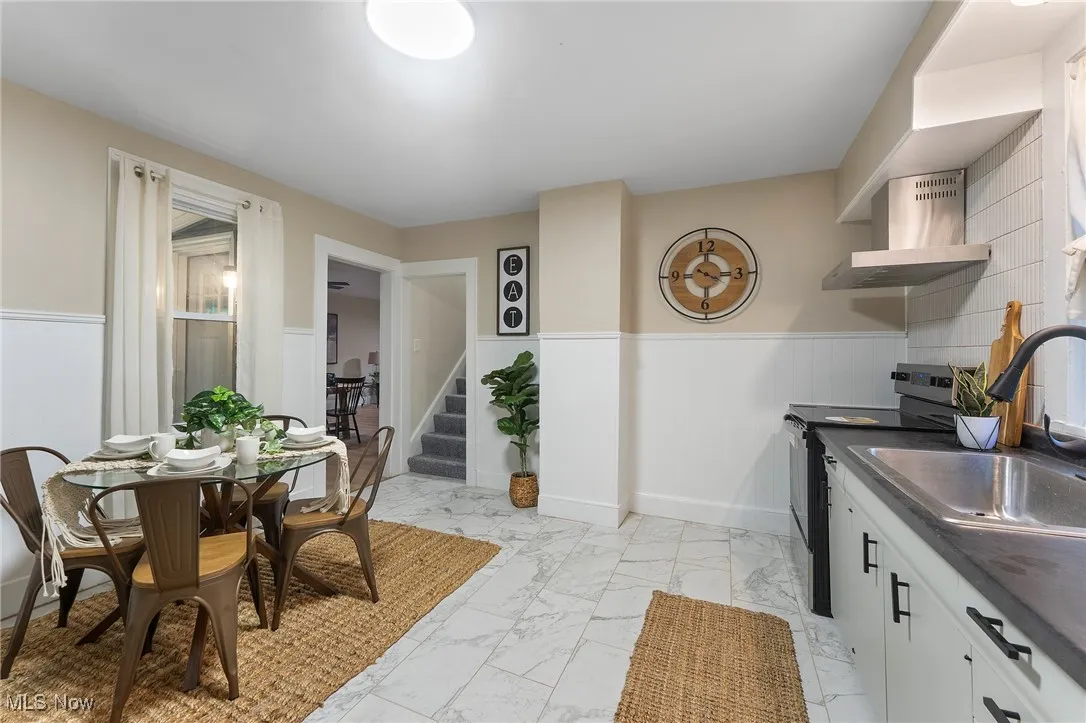 Dining space with light marble finish floors, a wainscoted wall, and stairs