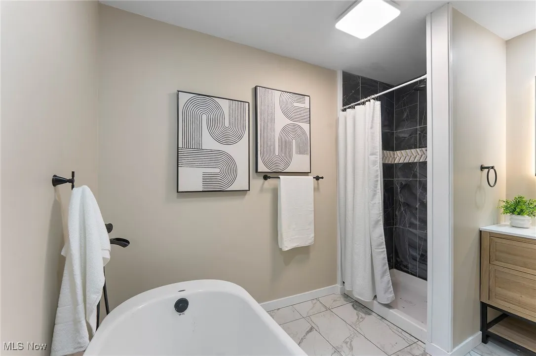 Bathroom with marble look tile flooring, a tile shower, a freestanding tub, and vanity