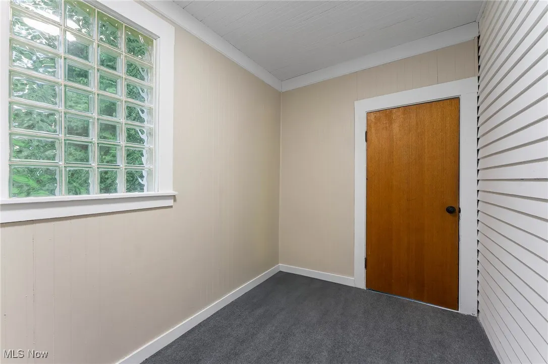Unfurnished room with dark colored carpet, wooden walls, and crown molding
