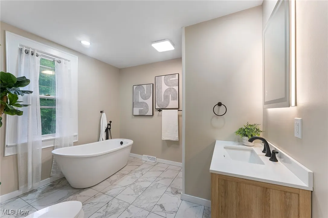 Full bath featuring vanity, marble finish flooring, a freestanding bath, and recessed lighting