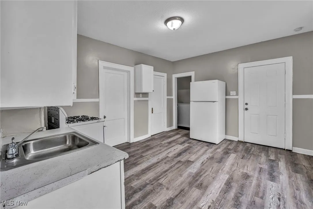 Kitchen featuring freestanding refrigerator, white cabinets, wood finished floors, and light countertops