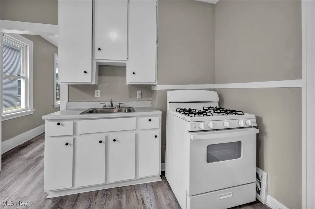 Kitchen with white range with gas stovetop, light countertops, white cabinets, and light wood-style floors