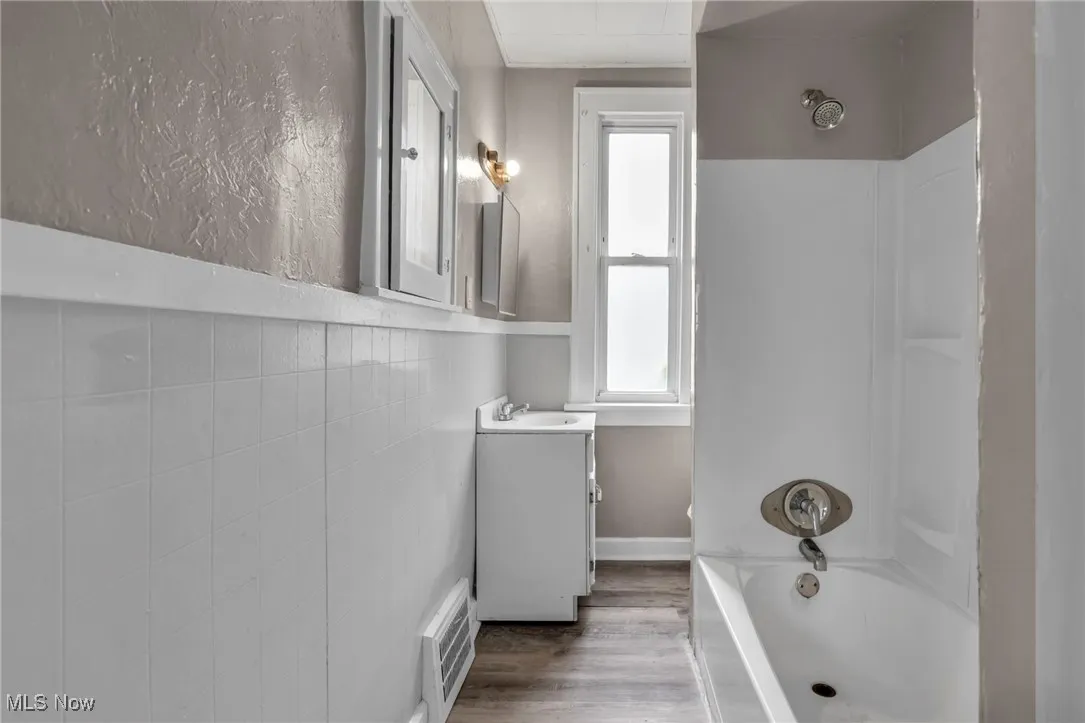 Bathroom with vanity, healthy amount of natural light, shower / washtub combination, and wood finished floors