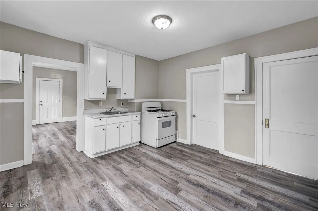 Kitchen with white gas range oven, white cabinetry, light countertops, and wood finished floors