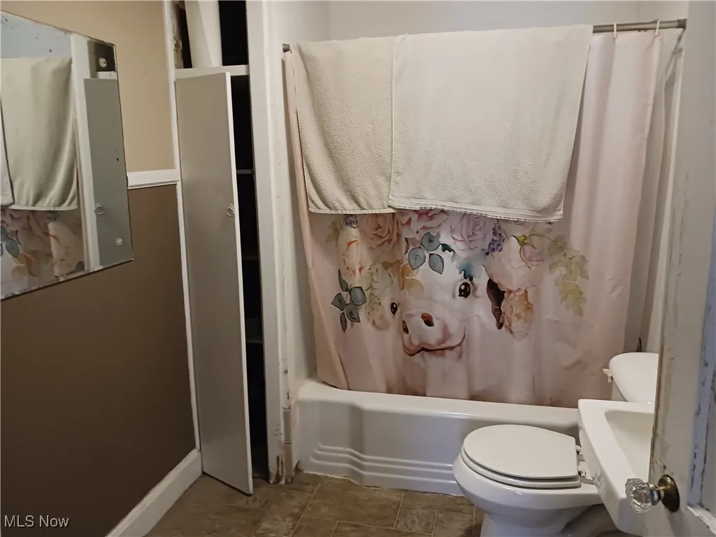 Bathroom with toilet and shower / tub combo with curtain