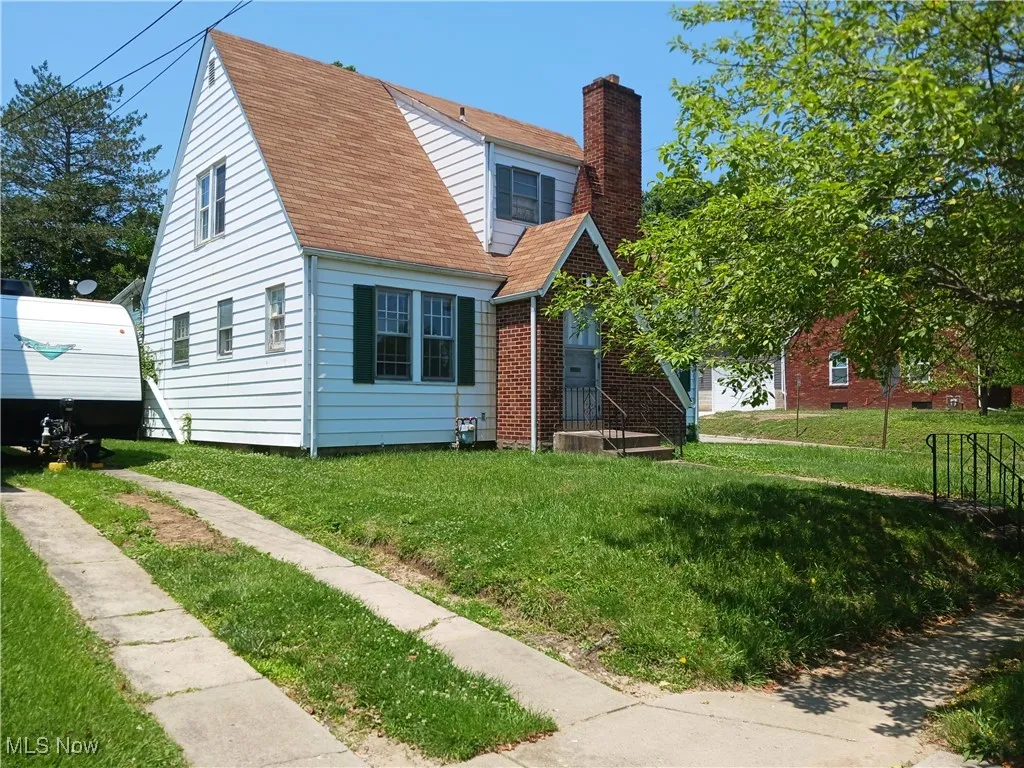 View of front of home with a chimney, a front yard, brick siding, and a shingled roof