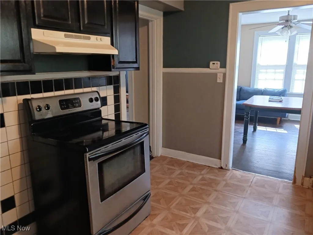Kitchen featuring stainless steel range with electric stovetop, under cabinet range hood, dark cabinets, and a ceiling fan