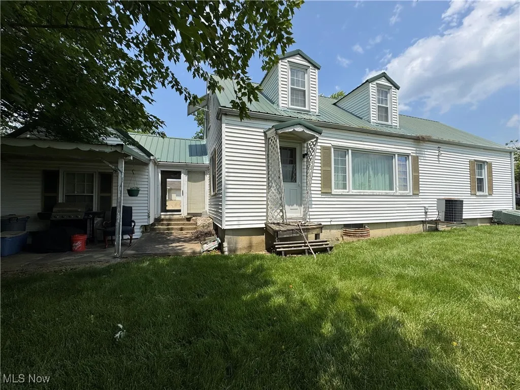 Back of house with entry steps, a lawn, metal roof, cooling unit, and a patio
