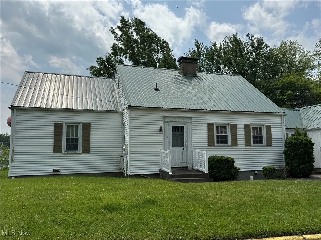 Rear view of house featuring a yard, a chimney, and metal roof