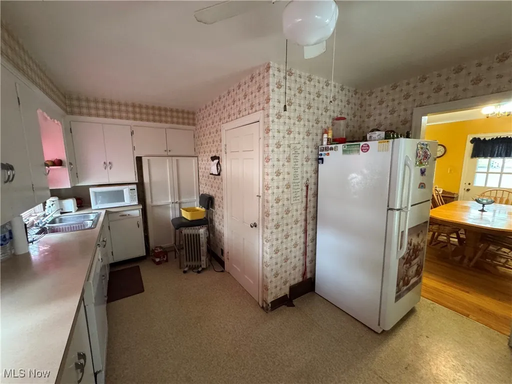 Kitchen featuring white appliances, wallpapered walls, a sink, light countertops, and white cabinets