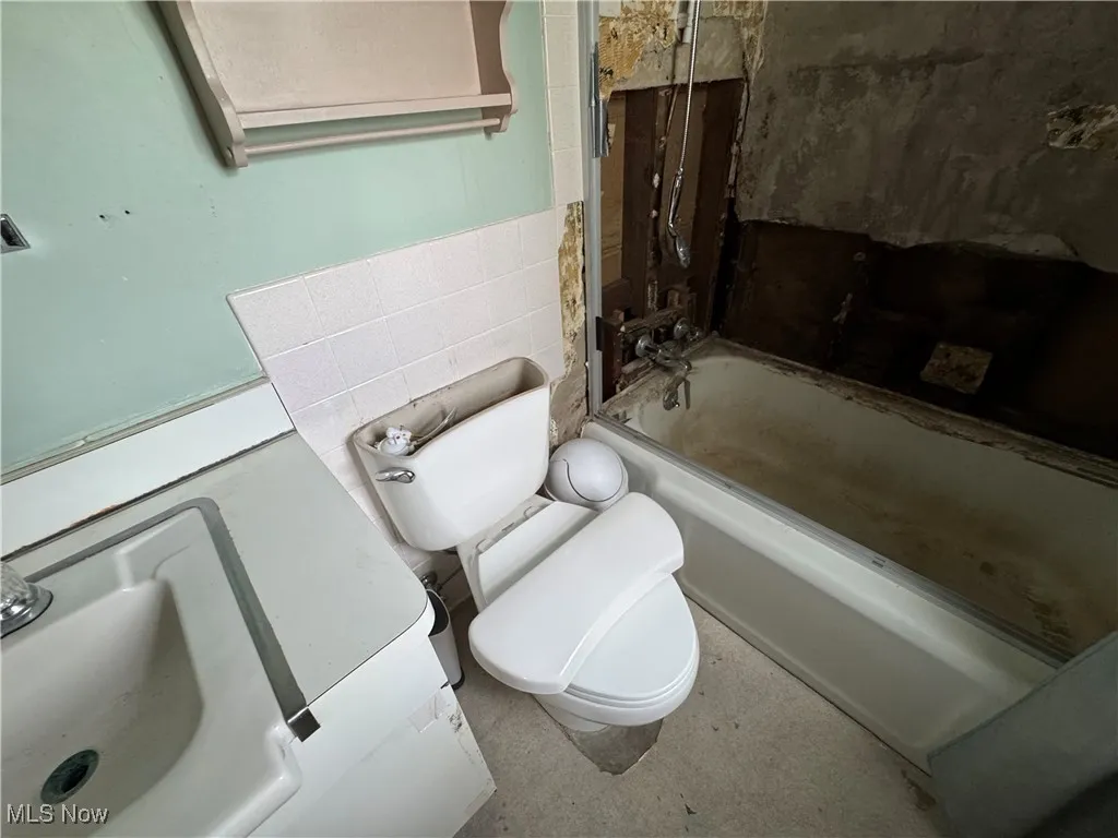 Bathroom with toilet, shower / tub combination, and tile walls