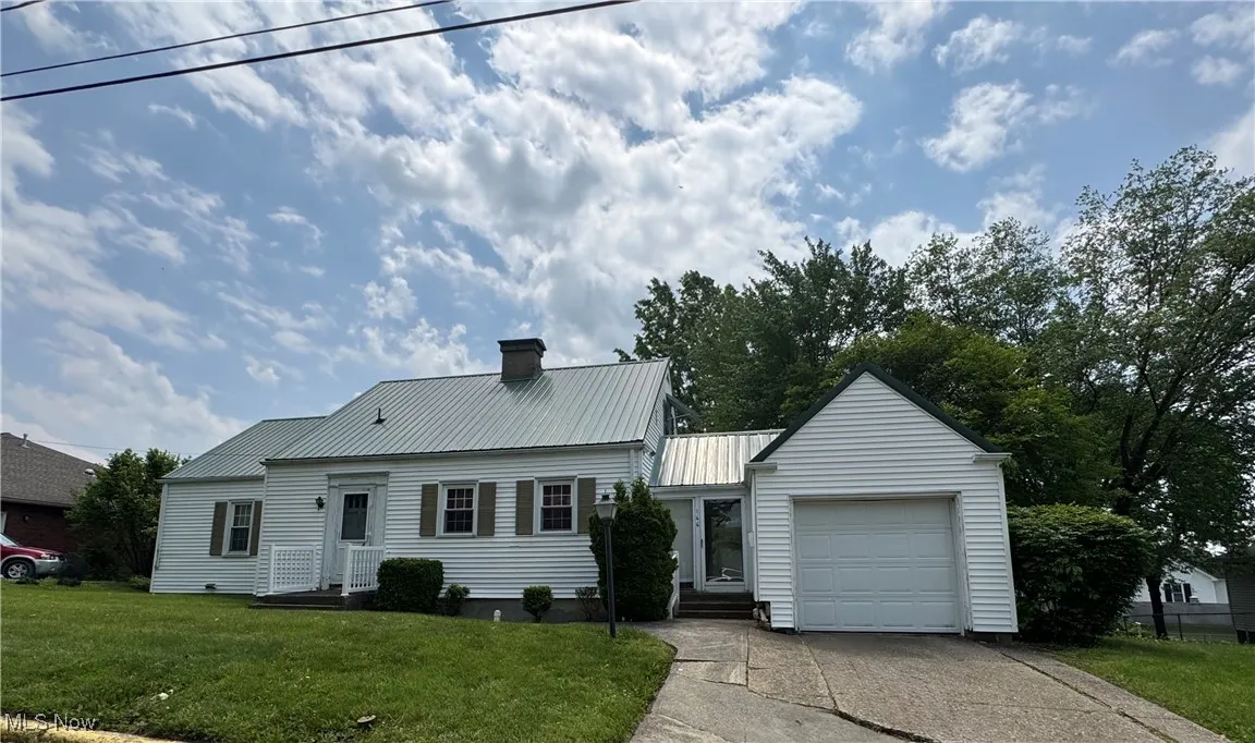 View of front of house with a chimney, a garage, metal roof, driveway, and a front yard