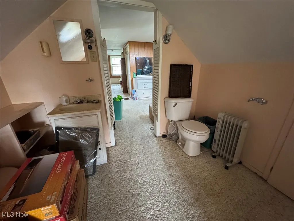 Bathroom with radiator heating unit, toilet, vaulted ceiling, and a sink