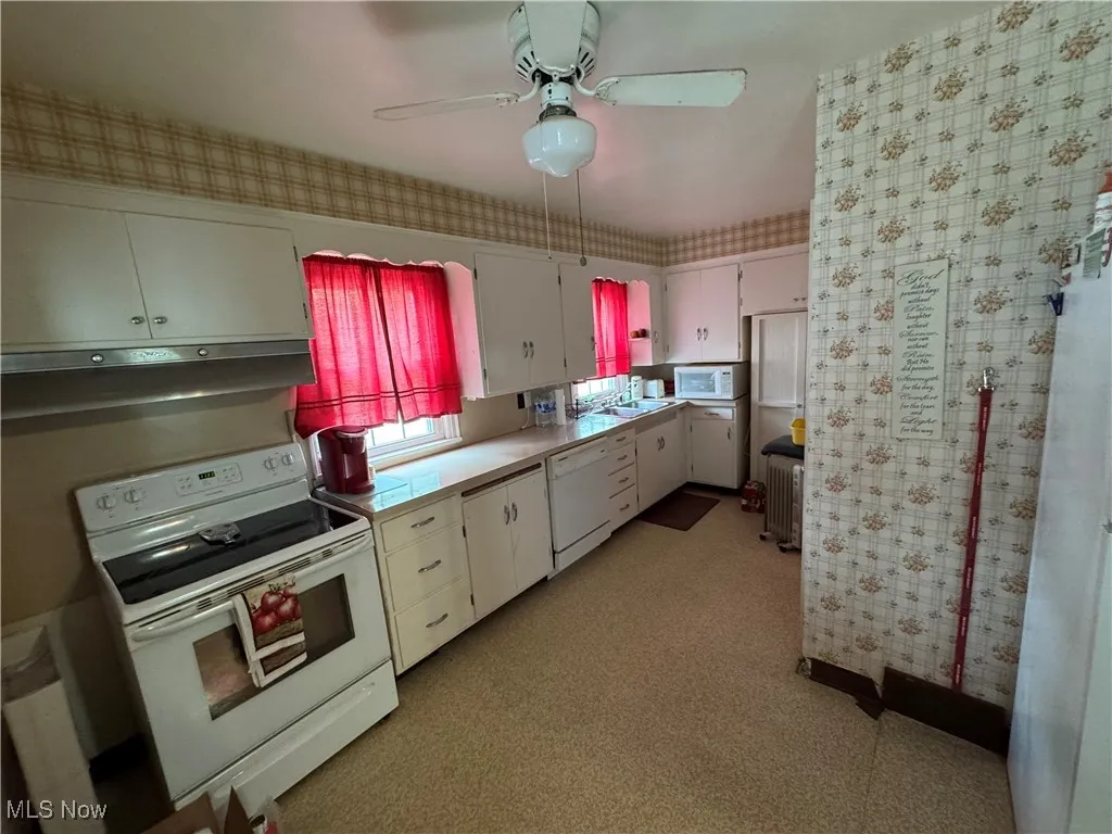 Kitchen with white appliances, wallpapered walls, white cabinetry, under cabinet range hood, and a ceiling fan