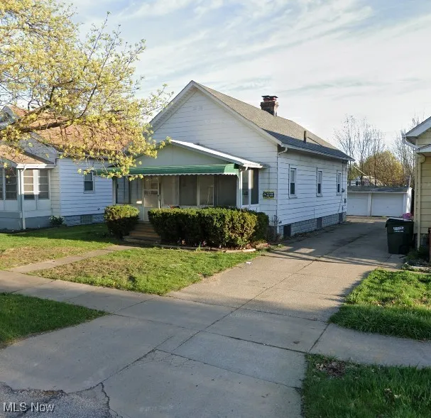 View of front of property featuring a front lawn, a detached garage, an outbuilding, a chimney, and roof with shingles