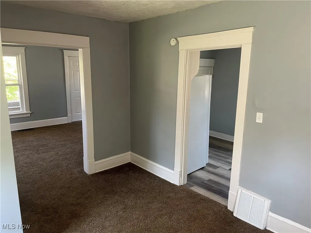 Spare room with dark carpet, a textured ceiling, and a smoke detector