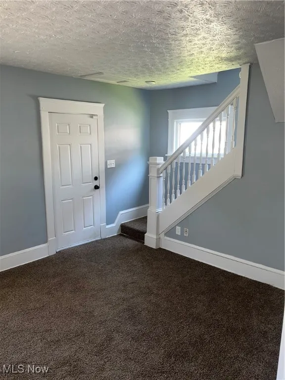 Entrance featuring a textured ceiling, carpet, and stairs