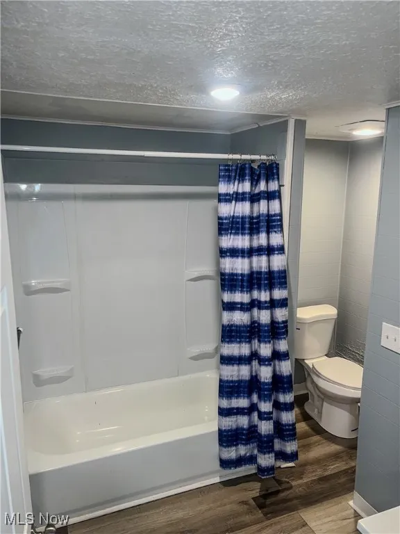 Bathroom with wood finished floors, a textured ceiling, and shower / tub combo with curtain