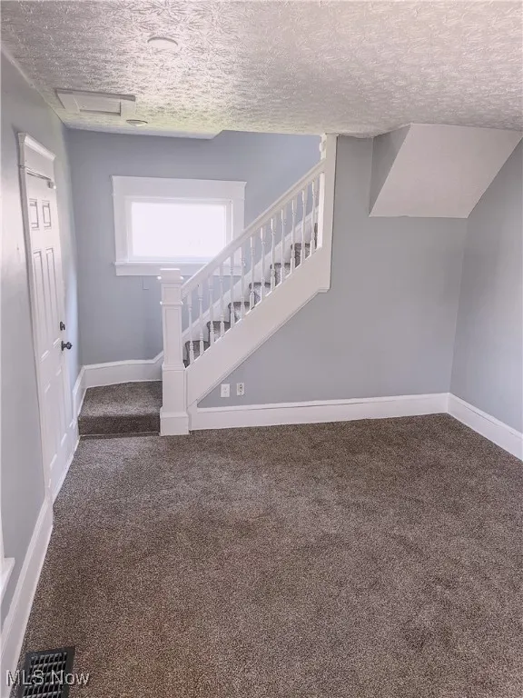 Living room area with carpet floors, a textured ceiling, and stairway