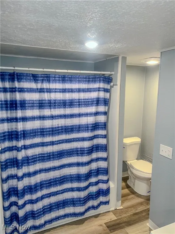 Full bath featuring a textured ceiling, wood finished floors, and a shower with shower curtain