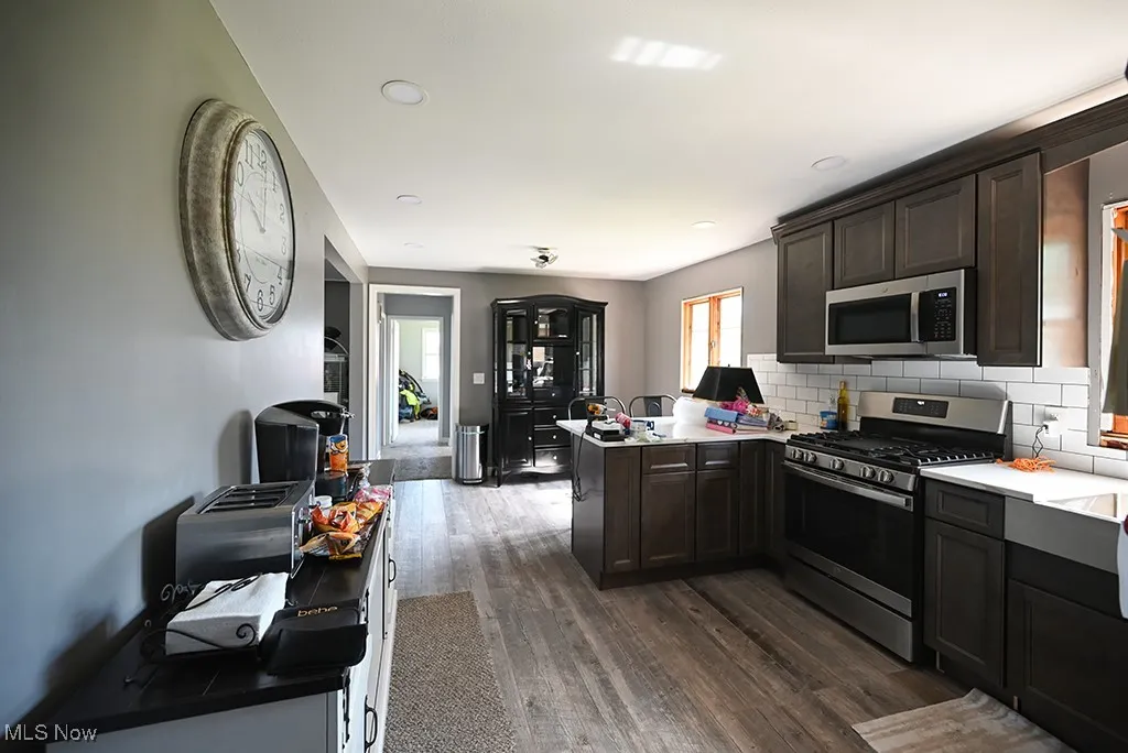 Kitchen with stainless steel appliances, a peninsula, dark brown cabinets, dark wood-style flooring, and backsplash