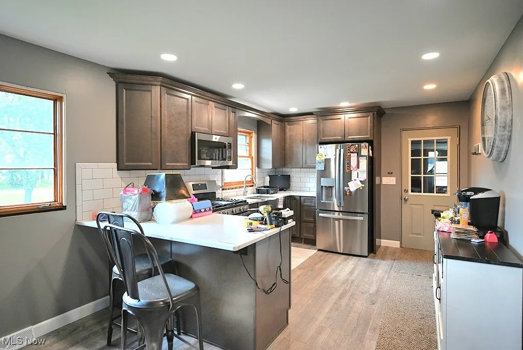 Kitchen featuring appliances with stainless steel finishes, a peninsula, light wood-type flooring, backsplash, and recessed lighting
