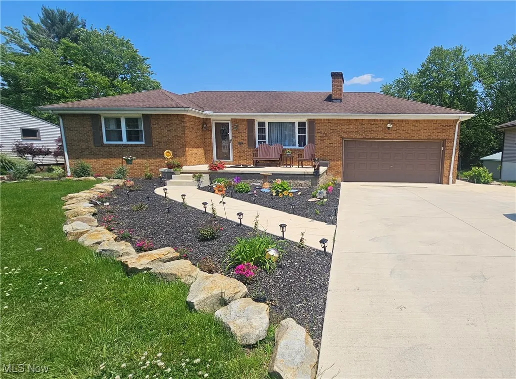 Ranch-style house featuring brick siding, a chimney, a front yard, driveway, and a garage