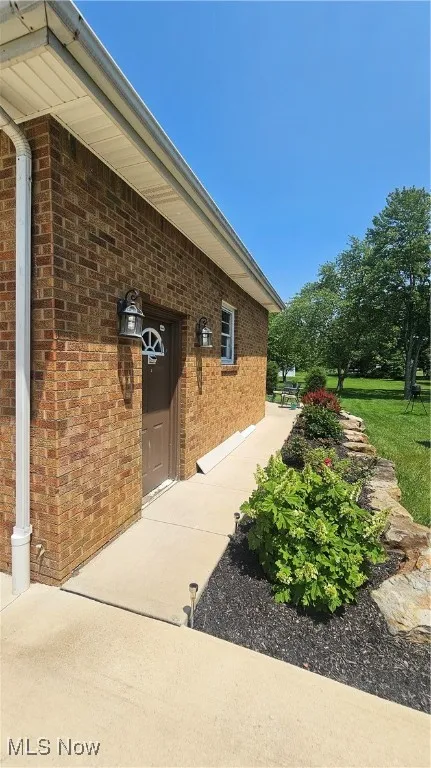 View of property exterior featuring brick and landscaping