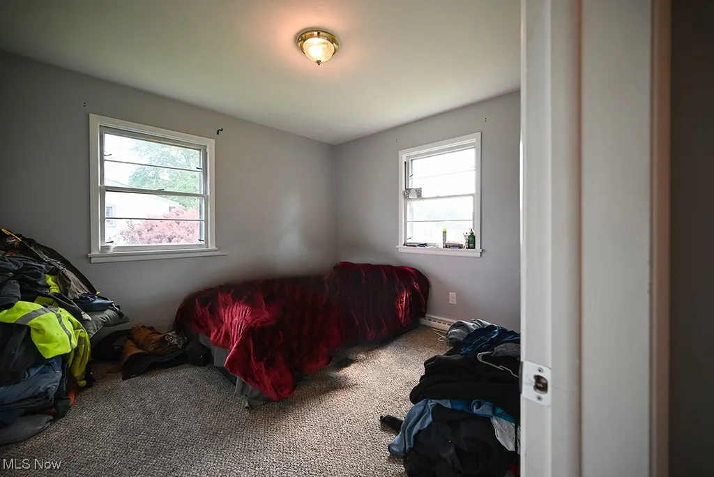 Carpeted bedroom featuring multiple windows and baseboard heating