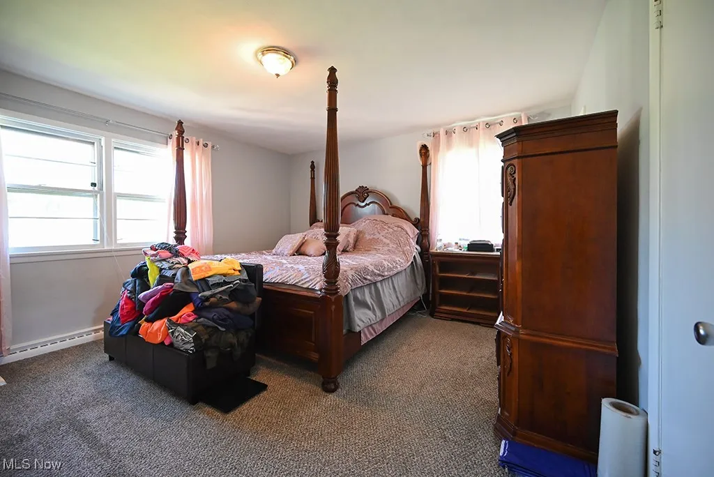 Bedroom with multiple windows, carpet flooring, and a baseboard heating unit