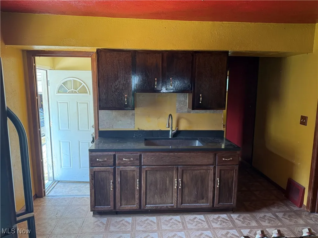 Kitchen with light floors, dark countertops, and dark brown cabinetry