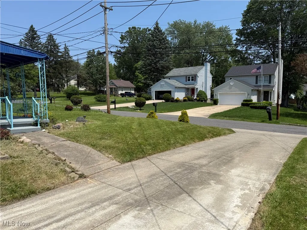 View of green lawn featuring covered porch, a garage, driveway, and a residential view